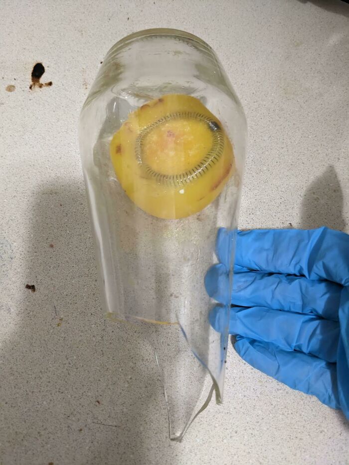 Curious thing discovered inside broken glass, with a coiled metal spring around yellow object, held by gloved hand.