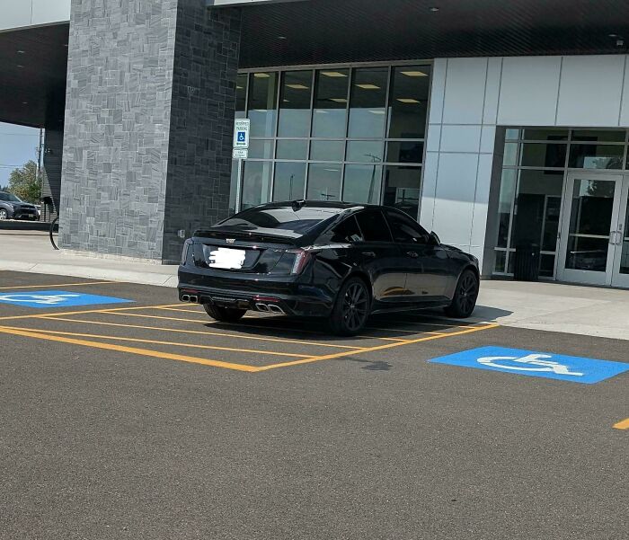 Black car illegally parked across two handicapped spots in front of a building, illustrating reasons why people hate their boss.