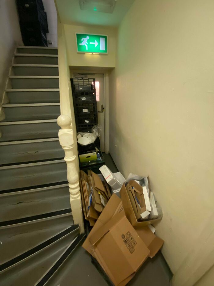 Cluttered stairwell and narrow exit blocked by cardboard boxes and crates, illustrating why people hate their boss.
