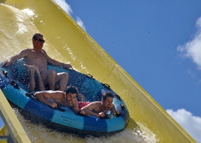 Three men enjoying a water ride on a large inflatable raft at an amusement park on a sunny day.