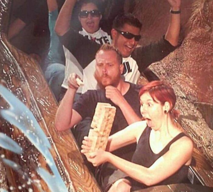 Four people riding a water log flume at an amusement park with one person holding Jenga blocks excitedly.