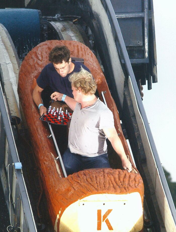 Two men playing chess on a log ride at an amusement park, capturing a unique memory from their trip.