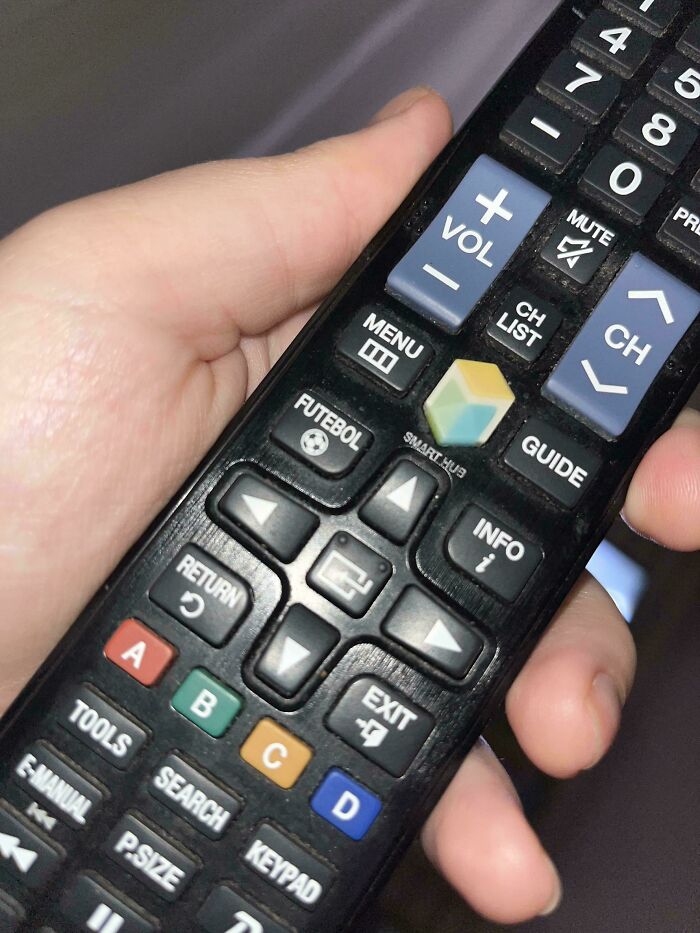 Close-up of a hand holding a TV remote featuring a colorful cube button, highlighting moderately interesting design details.