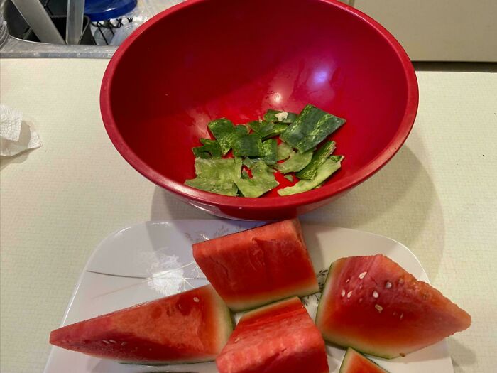 Watermelon slices on a plate next to a red bowl with watermelon rind pieces, showcasing moderately interesting food prep.