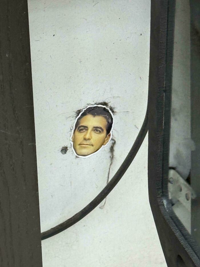 Sticker of a man's face partially torn on a wall with a cable running nearby, moderately interesting sight shared online.