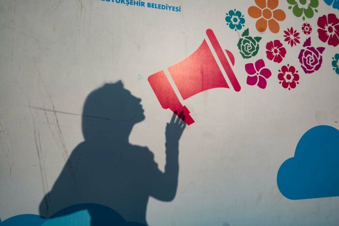 Shadow of a person appearing to shout into a red megaphone with colorful flowers, captured in perfectly timed street photo.