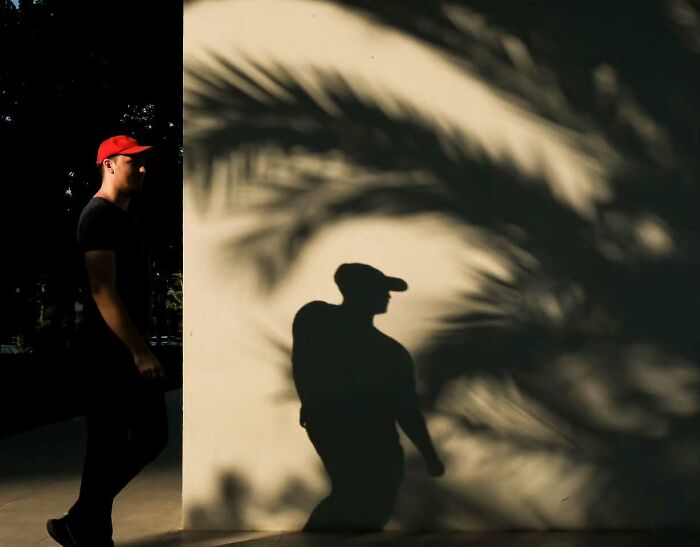 Man in red cap walking near wall with shadow resembling a perfectly timed street photo by photographer Melahat Ünel