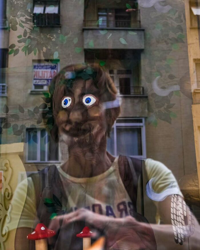 Distorted reflection of person with cartoonish eyes and red mushrooms, showcasing a perfectly timed street photo by Melahat Ünel.