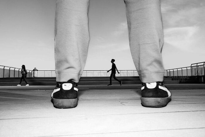 Black and white street photo showing a person’s legs and shoes framing a passerby, capturing a perfectly timed moment.