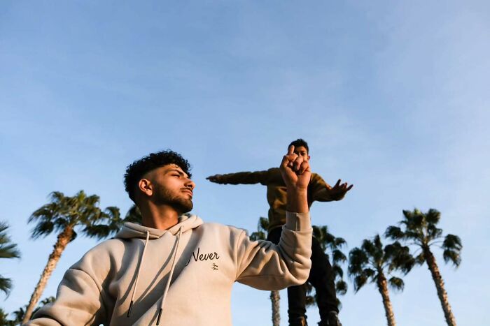 Two young men in casual clothes captured in a perfectly timed street photo with palm trees and clear sky background by Melahat Ünel.