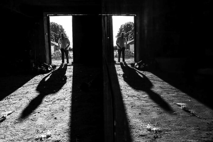 Man standing in a doorway casting long shadows reflected on a surface in a perfectly timed street photo.