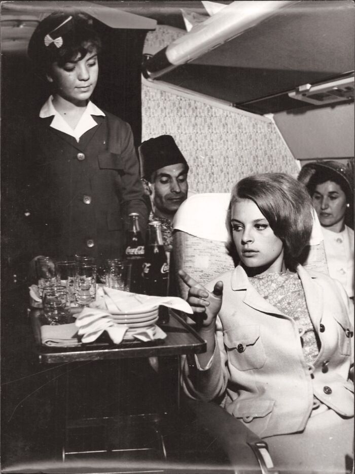 Vintage black and white photo showing people’s lives from a different time with a flight attendant serving drinks on a plane.