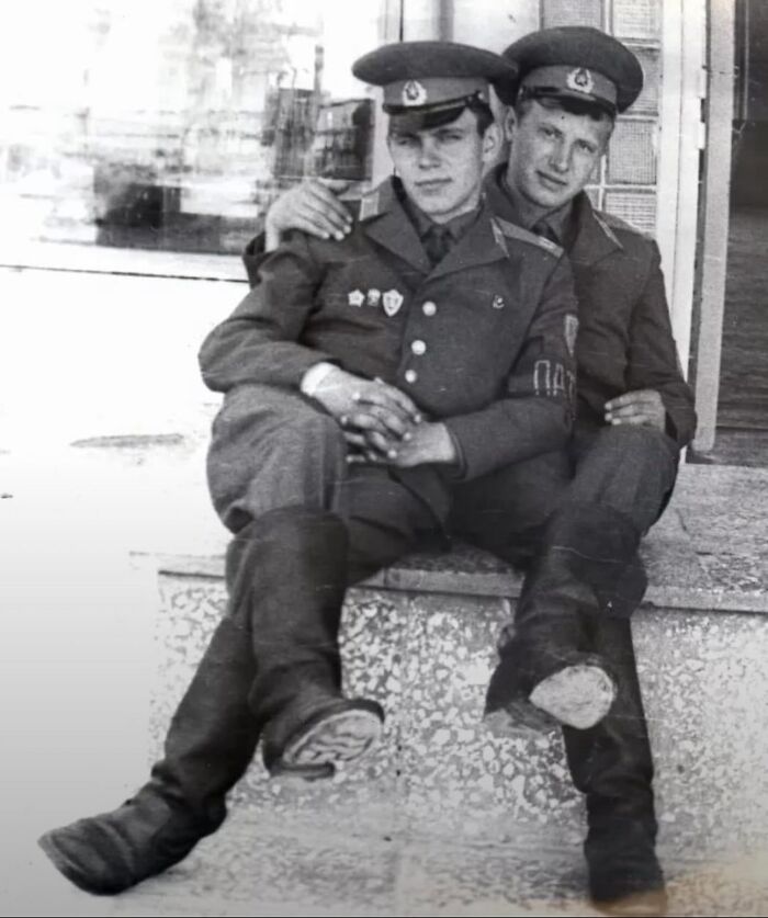 Two soldiers in uniform sitting closely on steps capturing old photos of lives from a different time.
