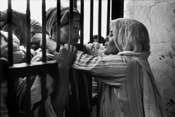 Black and white old photo showing emotional moment between people separated by prison bars, reflecting lives from a different time.