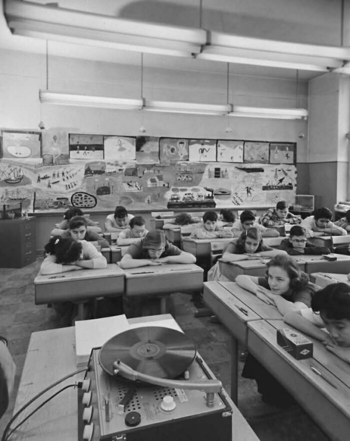 Old black and white photo of schoolchildren listening to a record player in a classroom showing people’s lives from a different time.