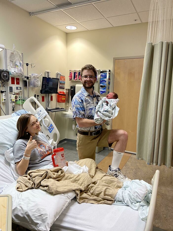 New parents in hospital room holding newborn baby, capturing a wholesome and cringe-worthy family moment.