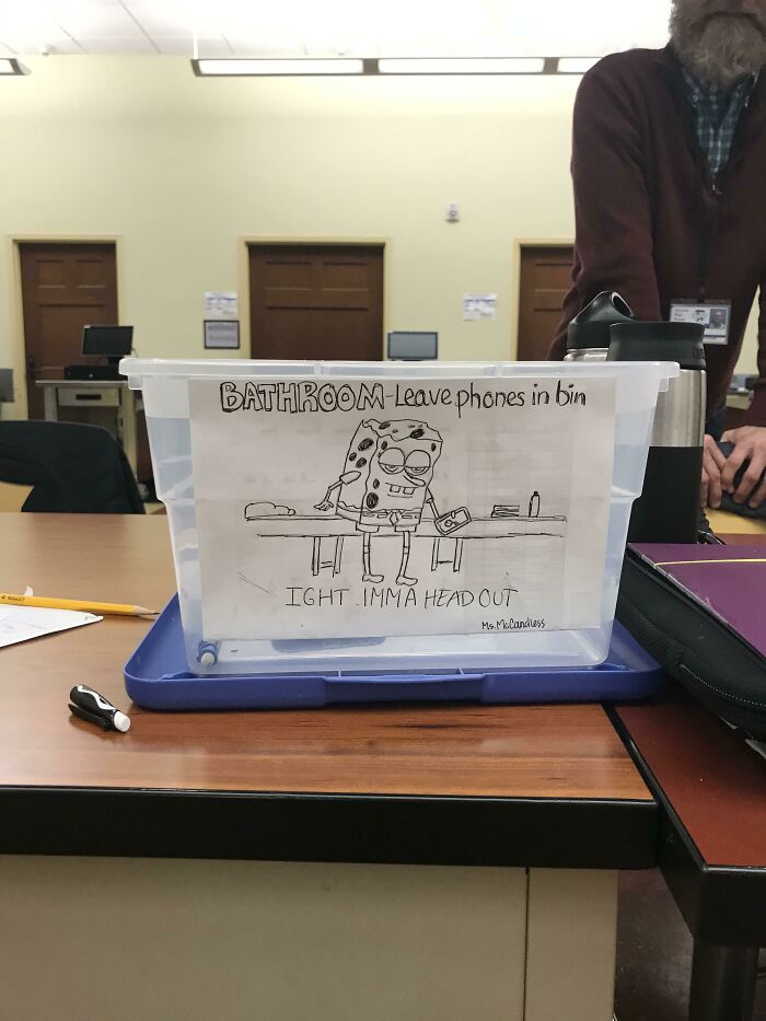 Plastic bin with a cringe-worthy but wholesome cartoon sign reminding to leave phones in bin before bathroom use.