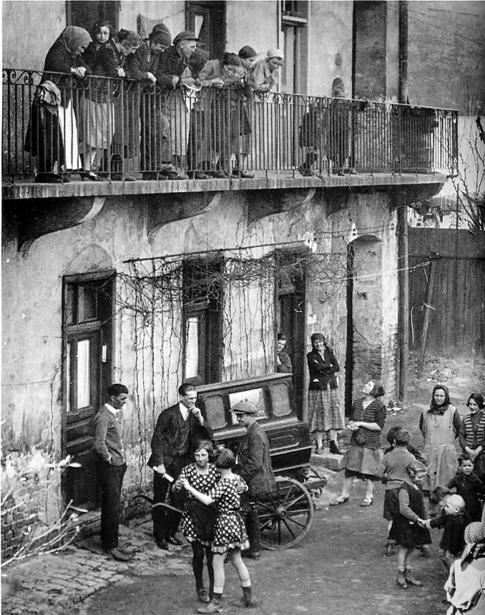 Group of people in an old black and white photo showing lives from a different time on a street and balcony.