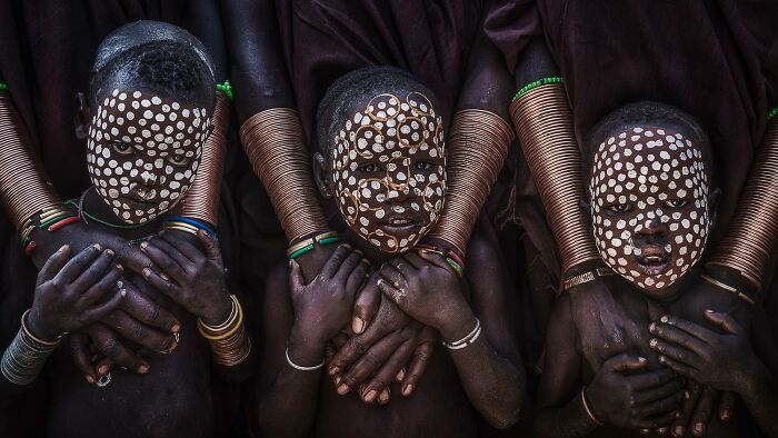 Three children with intricate white face paint and colorful bracelets, showcasing revealing Earth's hidden patterns in photography.
