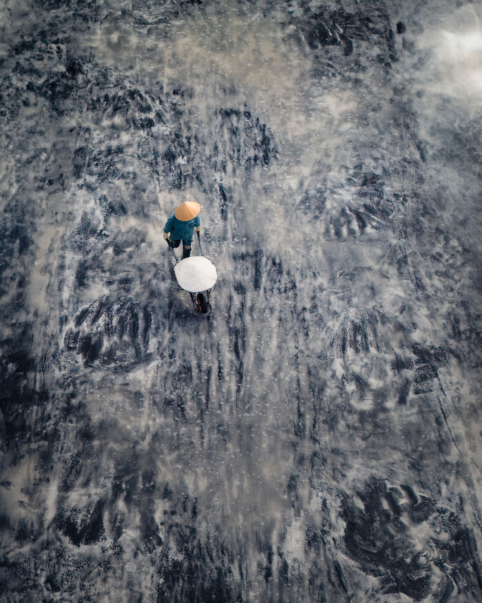 Aerial color photography showing a worker pushing a cart on textured earth revealing hidden patterns.