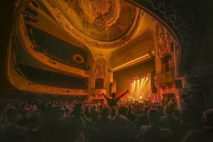 Audience enjoying a live concert inside an ornate theater, showcasing vibrant aerial color photography patterns.