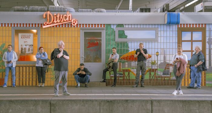 Group of people waiting on a platform with colorful tiled wall showcasing Earth’s hidden patterns in aerial photography style