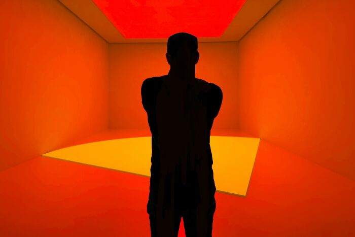Silhouette of person standing in a room with vibrant orange and yellow lighting showcasing hidden earth patterns.