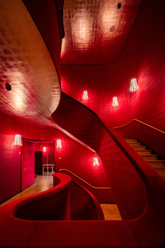 Curving red staircase with glowing wall lights showcasing stunning aerial color photography patterns in a vibrant interior setting.