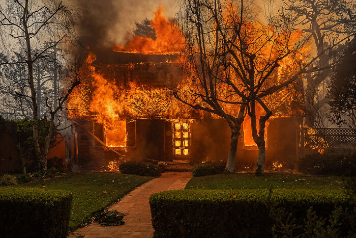 House engulfed in flames with intense fire and smoke, revealing earth’s hidden patterns from an aerial color photography perspective.