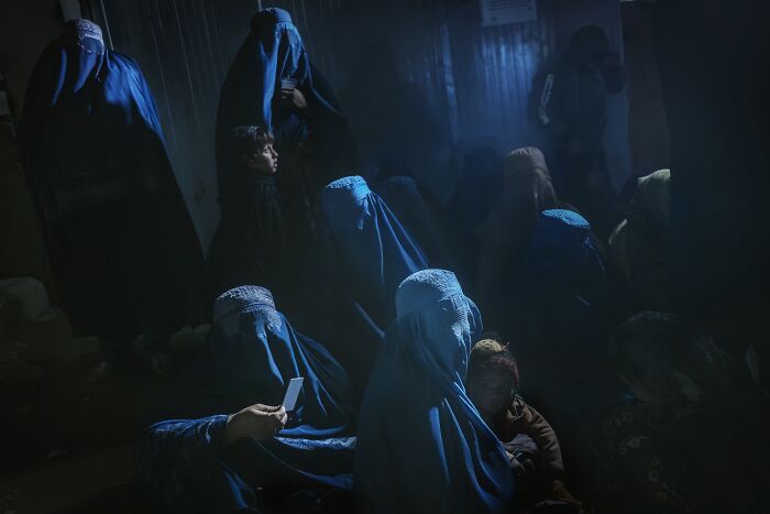 Dark indoor scene of women in blue burqas and children, showcasing revealing Earth’s hidden patterns through aerial color photography.