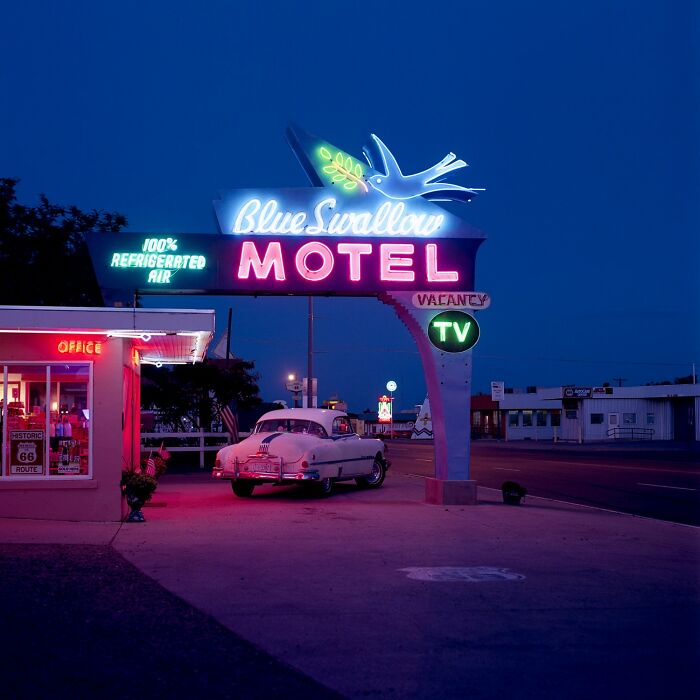 Vintage car parked under neon Blue Swallow Motel sign at night, showcasing stunning aerial color photography patterns.