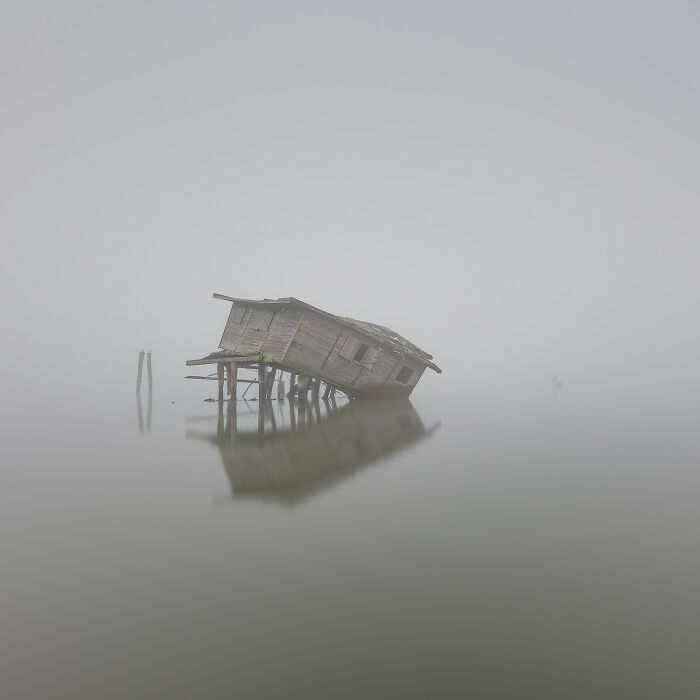Abandoned wooden shack reflected in calm water surrounded by mist, showcasing Earth's hidden aerial patterns.