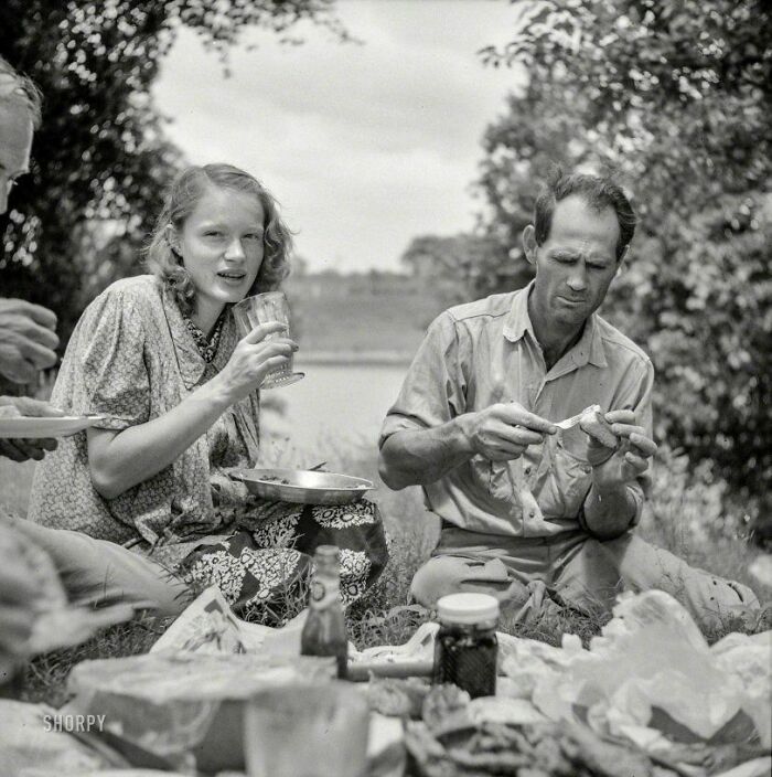 Black and white old photo of people having a picnic outdoors, capturing everyday life from a different time period.