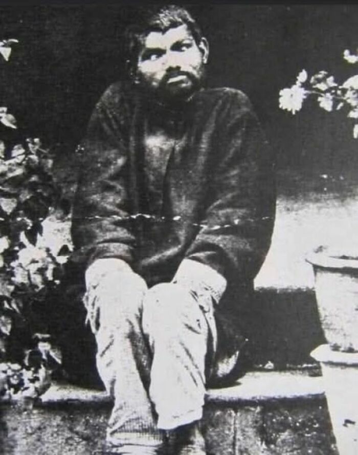 Black and white old photo showing a man sitting on steps, reflecting the lives of people from a different time period.