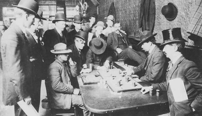 Group of men in period clothing playing board games in an old photo capturing people’s lives from a different time.