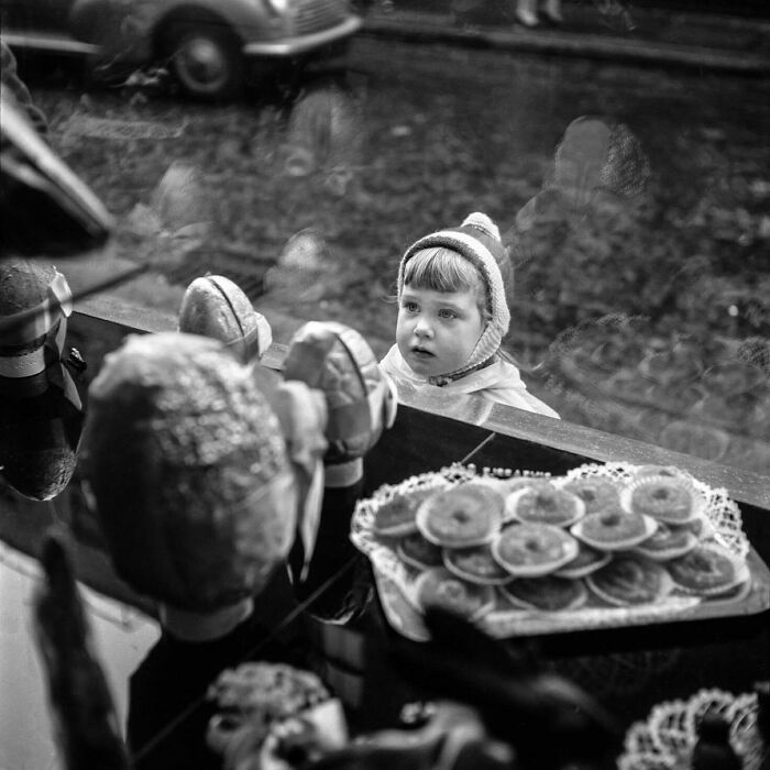Black and white photo showing a child looking through a shop window in an old photo capturing people's lives from a different time.
