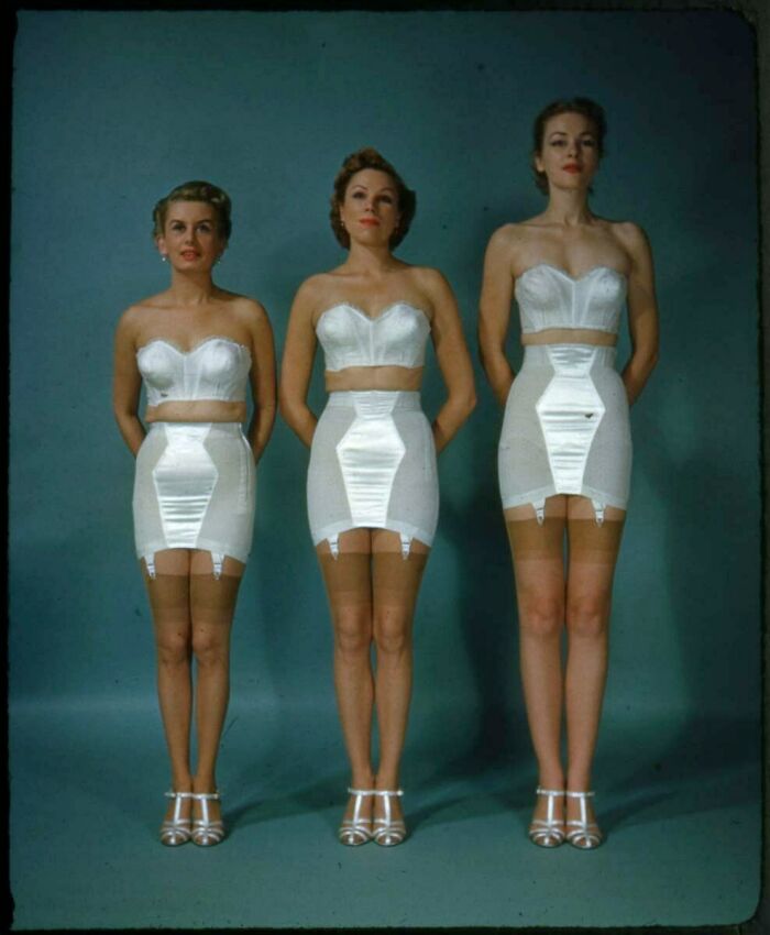 Three women in vintage undergarments and heels, showcasing old fashion from a different time in black and white photography.