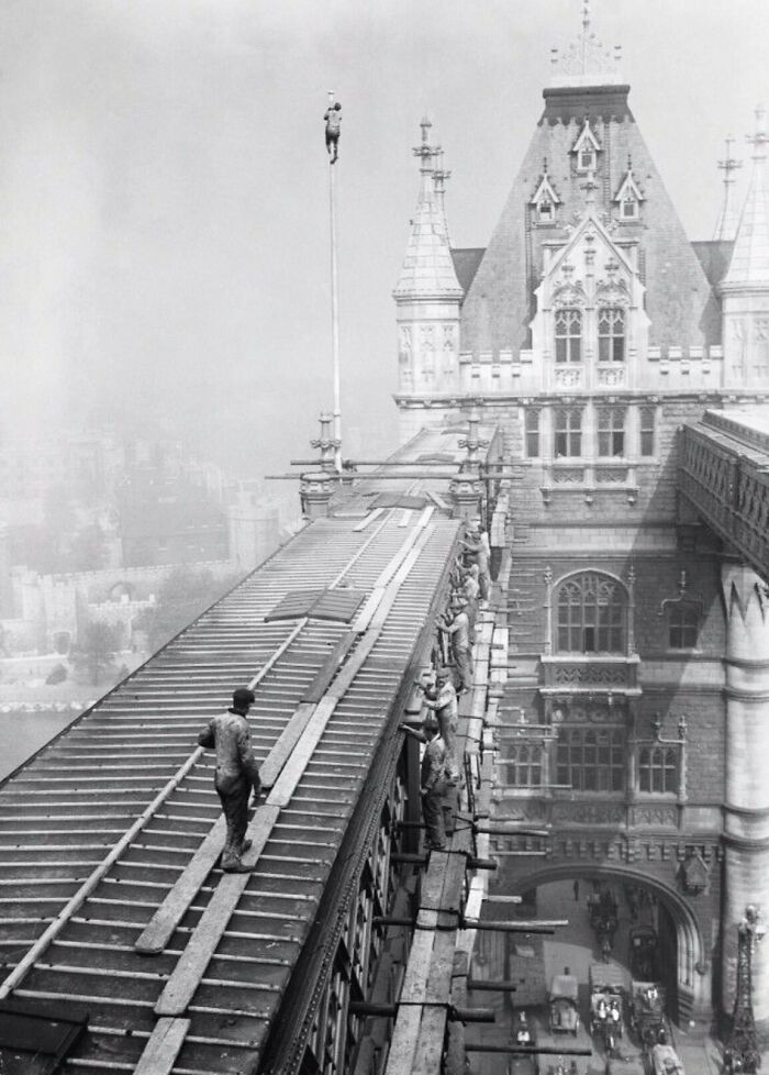 Old photo of construction workers on a bridge roof, showcasing people’s lives and labor from a different time period.