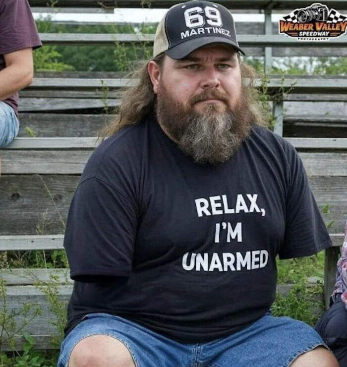 Bearded man wearing a funny shirt sitting on wooden bleachers in funny and bizarre image combining the holy and the cursed.