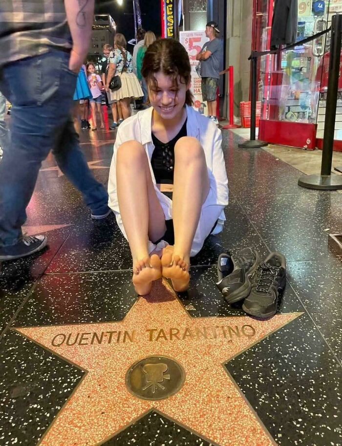 Young woman sitting barefoot on a Hollywood Walk of Fame star, surrounded by people and shoes nearby, funny and bizarre image.