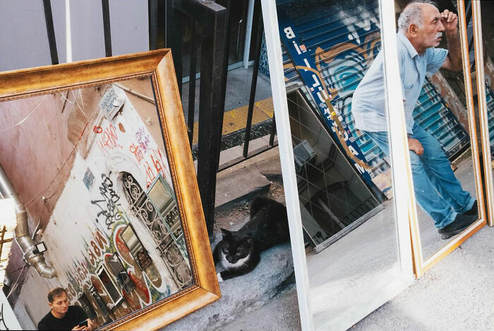 Three large mirrors on the street reflecting graffiti, a cat, and an elderly man in a candid moment in Turkey.