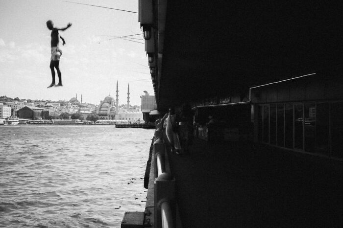 Boy jumping into the water under a bridge, showcasing the real, candid side of life in Turkey by Yusuf Aksoy.