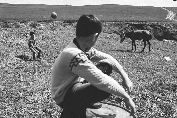 Black and white photo showing candid life in Turkey with two boys playing near a horse in an open rural field.