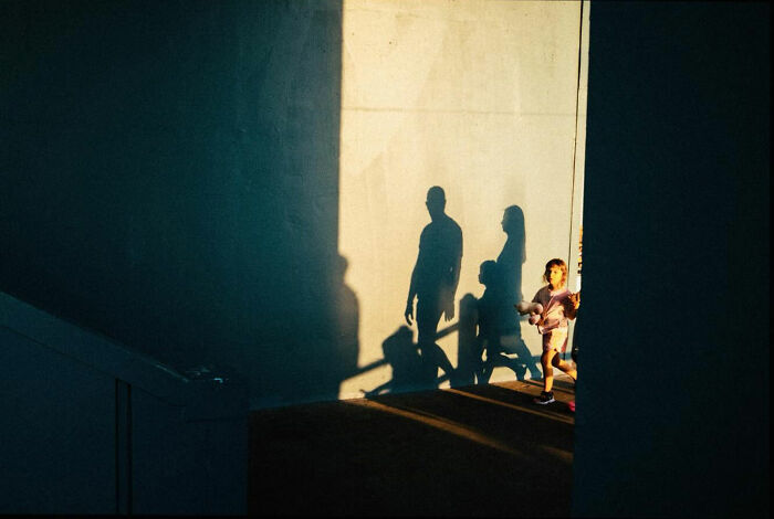 Child walking with shadows of people cast on a wall, showcasing the real candid side of life in Turkey by Yusuf Aksoy.