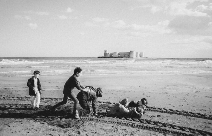 Children playing on a beach in Turkey near a historic castle, showcasing the real candid side of life in Turkey by Yusuf Aksoy.