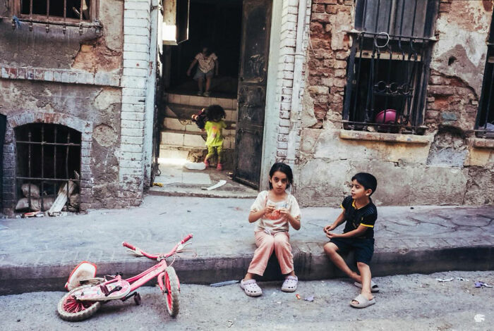Children sitting and playing outside a worn building in Turkey, showcasing the real candid side of life through photography.