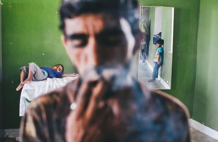 Man smoking a cigarette with two children in a green-walled room, capturing the real, candid side of life in Turkey.