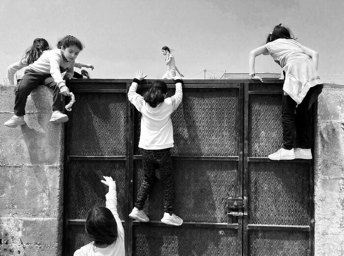 Children climbing and playing on a metal gate, showcasing the real, candid side of life in Turkey in black and white.