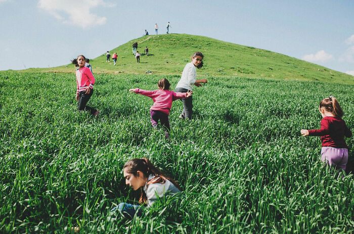 Children playing in a green field on a sunny day, showcasing the real candid side of life in Turkey by Yusuf Aksoy.
