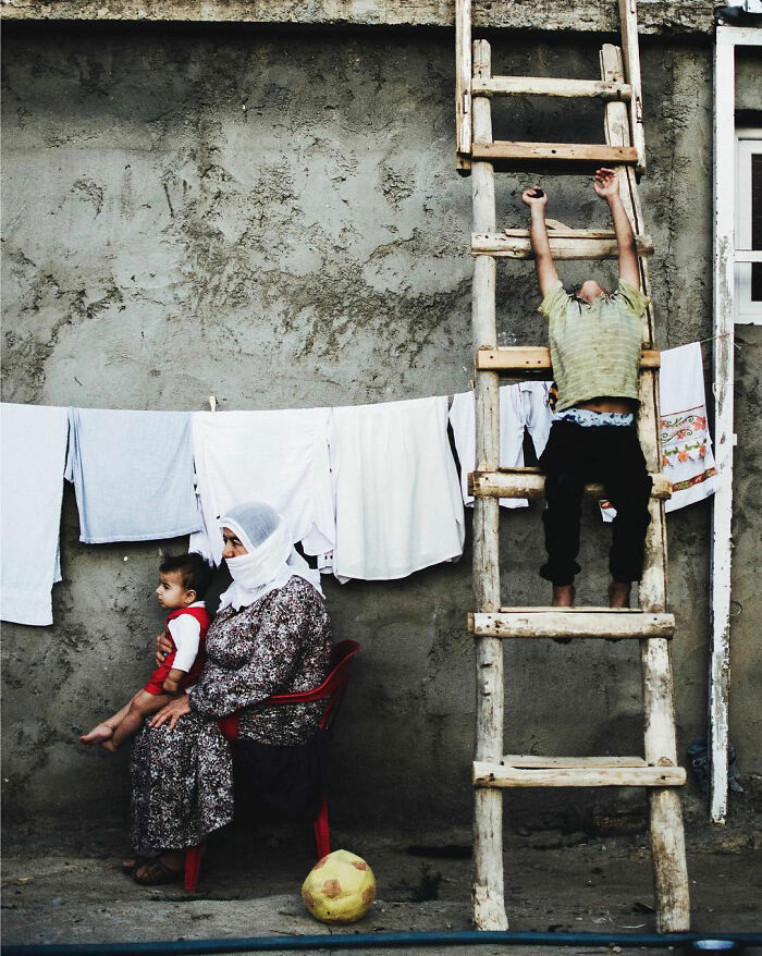 Elderly woman holding a child by a clothesline while a boy climbs a wooden ladder in a candid Turkey life photo.